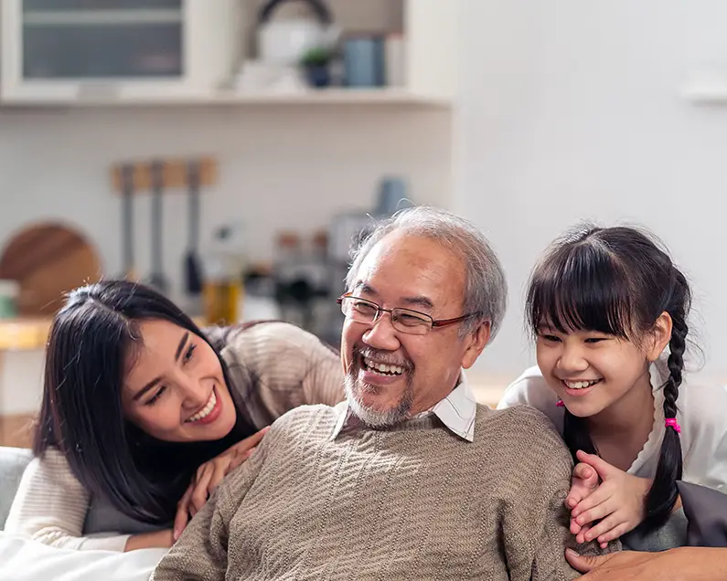 Multigenerational Caucasian family with grandfather, mom, dad and young daughter and son sitting on a couch smiling.